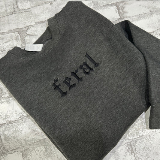 Dark Gray sweatshirt with black embroidered gothic text reading “feral” on the chest.