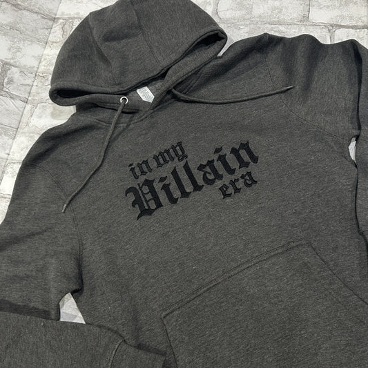 A dark gray hoodie with the phrase 'In My Villain Era' embroidered in black on the front.