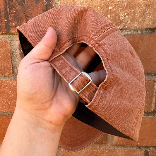 Back view of a distressed baseball cap showing adjustable fabric strap with metal buckle closure.