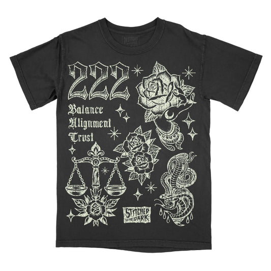 black T-shirt featuring a distressed 222 angel number design with roses, a mystical hand, balance scales, snakes, and stars, with text reading “Balance,” “Alignment,” and “Trust,” plus Stitched in the Dark branding.