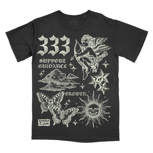 black T-shirt featuring a distressed 333 angel number design with a cherub, butterflies, clouds, stars, and a skull sun, with text reading “Support Guidance” and “Growth” and Stitched in the Dark branding.