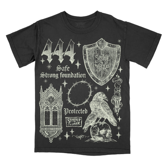black T-shirt featuring a distressed 444 angel number design with a medieval shield, gothic window, barbed wire halo, raven perched on a skull, and candle, with text reading “Safe,” “Strong Foundation,” and “Protected,” plus Stitched in the Dark branding.