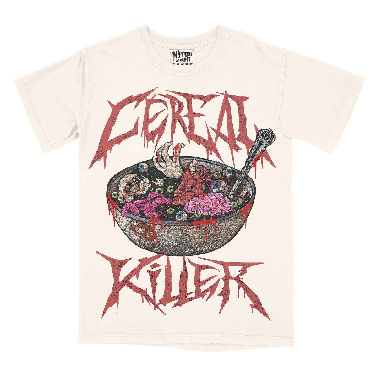 Cream graphic t-shirt featuring the phrase “Cereal Killer” in jagged, horror-style lettering above and below an illustration of a cereal bowl filled with eyeballs, brains, and bloody details, with a spoon dripping red liquid.