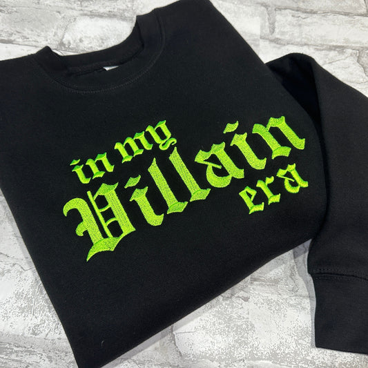 Black crewneck sweatshirt with green embroidered text 'in my Villain era' on the front.