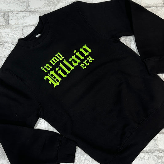 Black crewneck sweatshirt with green embroidered text 'in my Villain era' on the front.