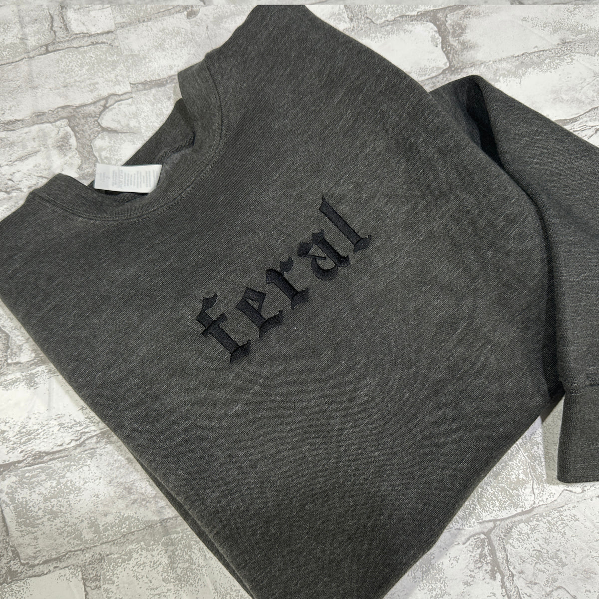 Dark Gray sweatshirt with black embroidered gothic text reading “feral” on the chest.