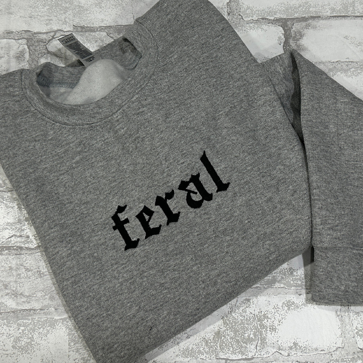 Gray embroidered gothic text reading “feral” on the chest.