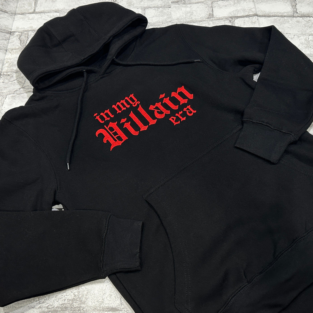 Black hoodie with 'in my Villain era' text embroidered in red on the front.