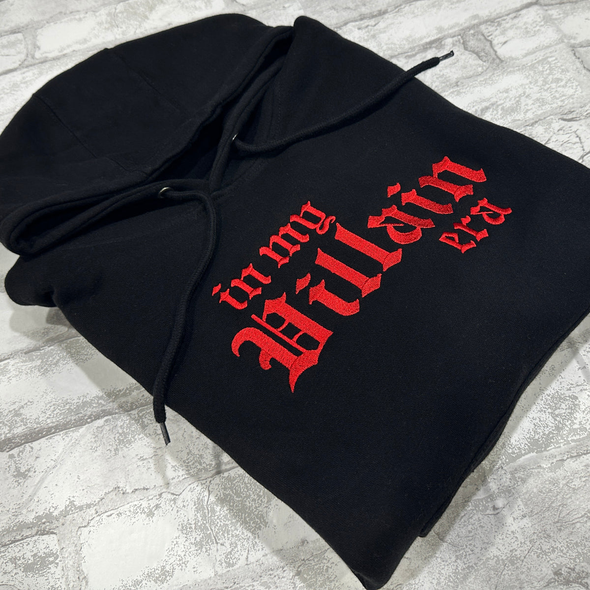 Black hoodie with 'in my Villain era' text embroidered in red on the front.