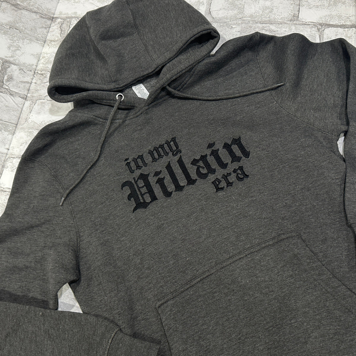 A dark gray hoodie with the phrase 'In My Villain Era' embroidered in black on the front.