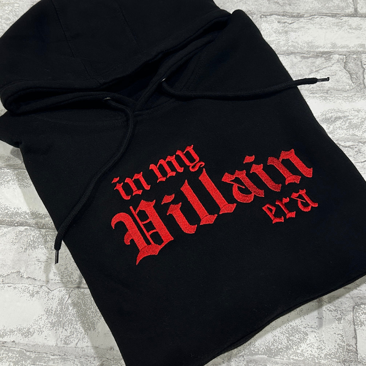Black hoodie with 'in my Villain era' text embroidered in red on the front.