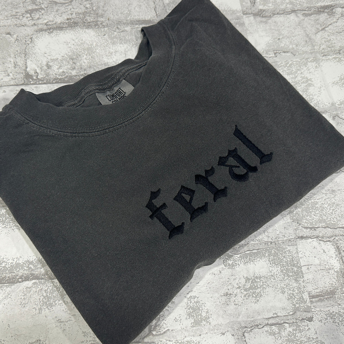 A pepper embroidered t-shirt with the word 'feral' written in bold letters across the front.