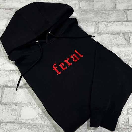 A black hoodie with the word 'feral' embroidered in red on the front.