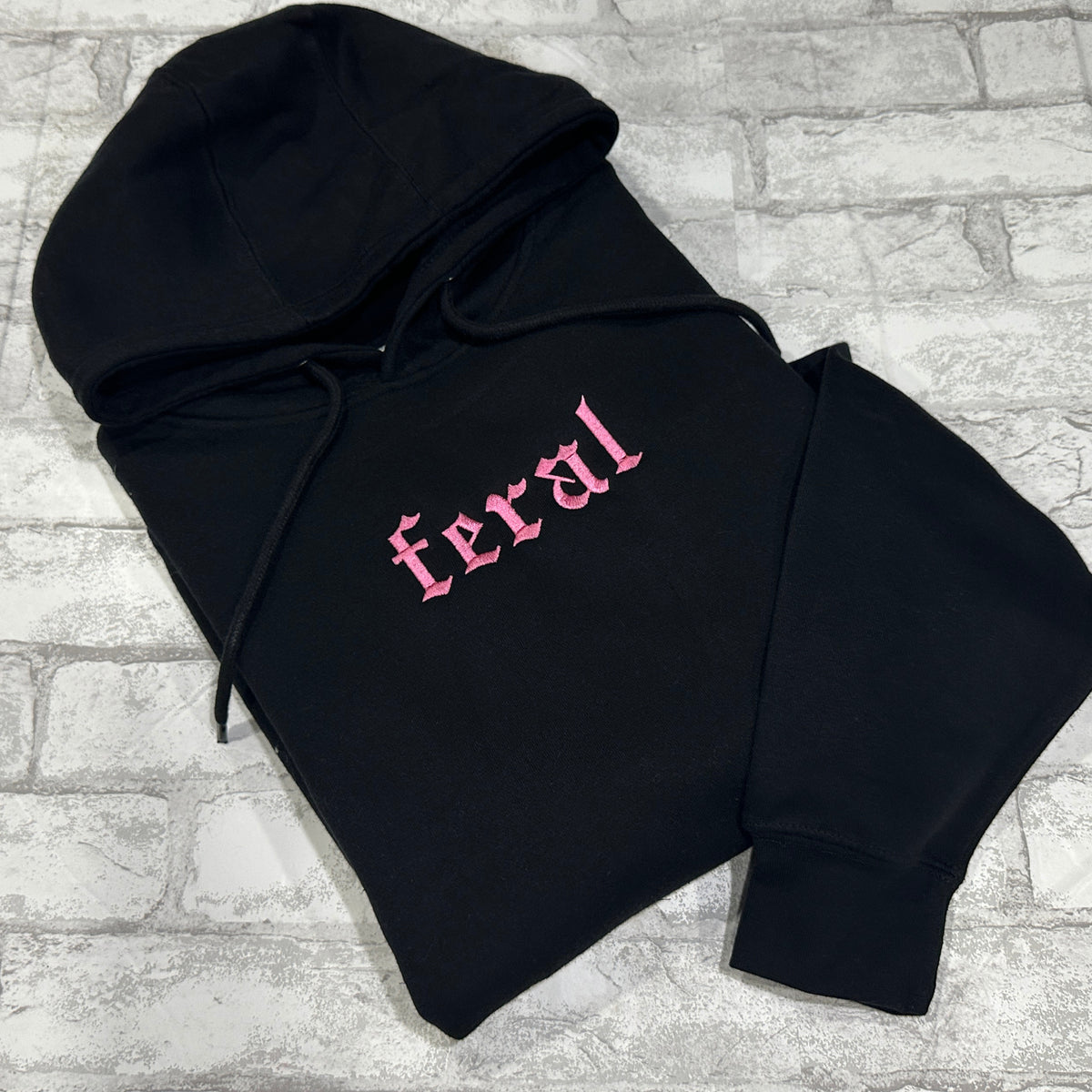 A black hoodie with the word 'feral' embroidered in pink on the front.