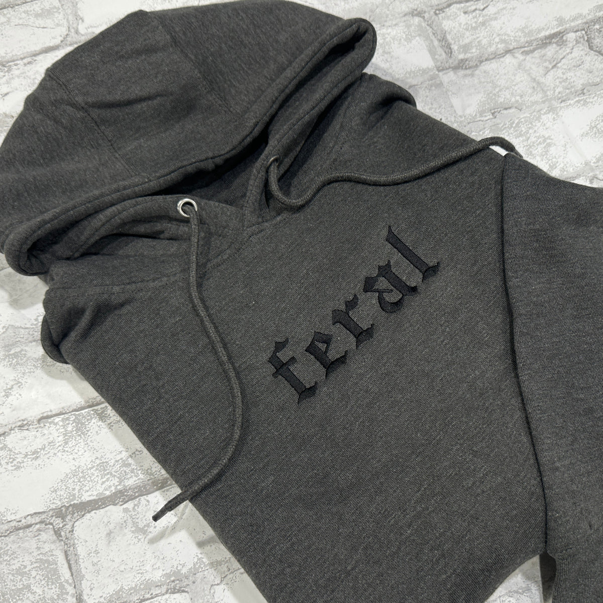 A dark gray hoodie with the word 'feral' embroidered in black on the front.