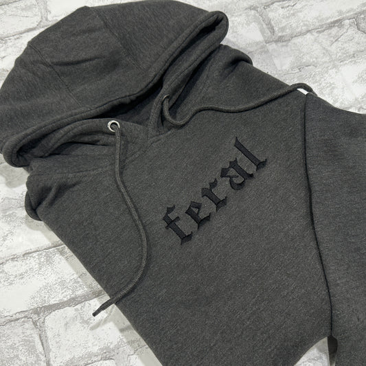 A dark gray hoodie with the word 'feral' embroidered in black on the front.