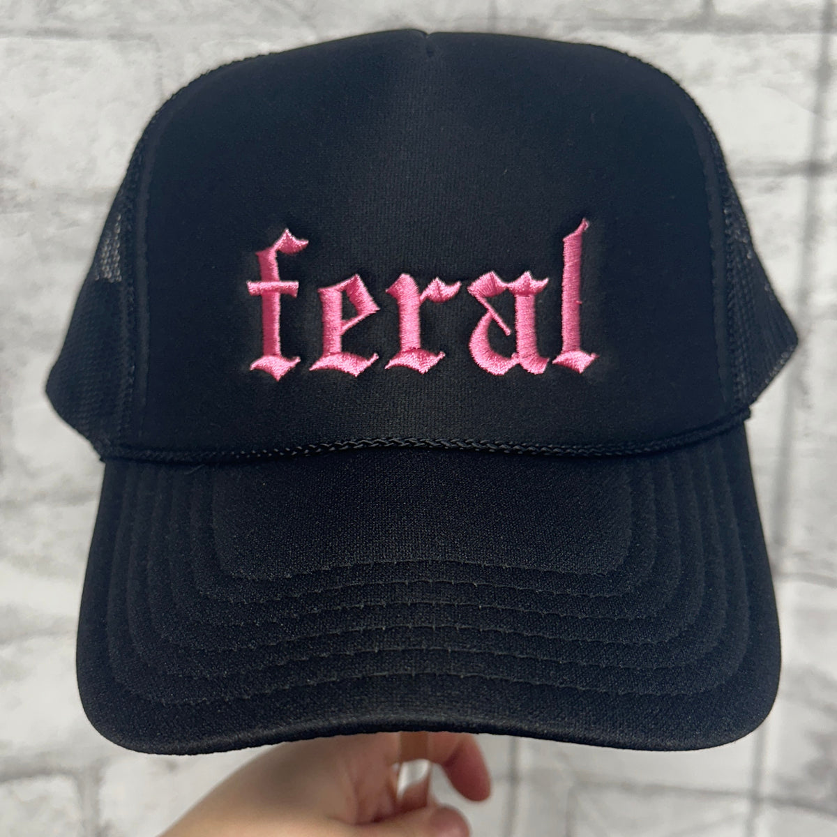 Black mesh trucker hat with pink embroidered “feral” text on the front.