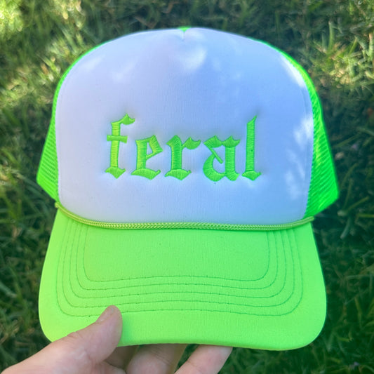 Front view of a neon green and white mesh trucker hat with green embroidered text reading “feral.”