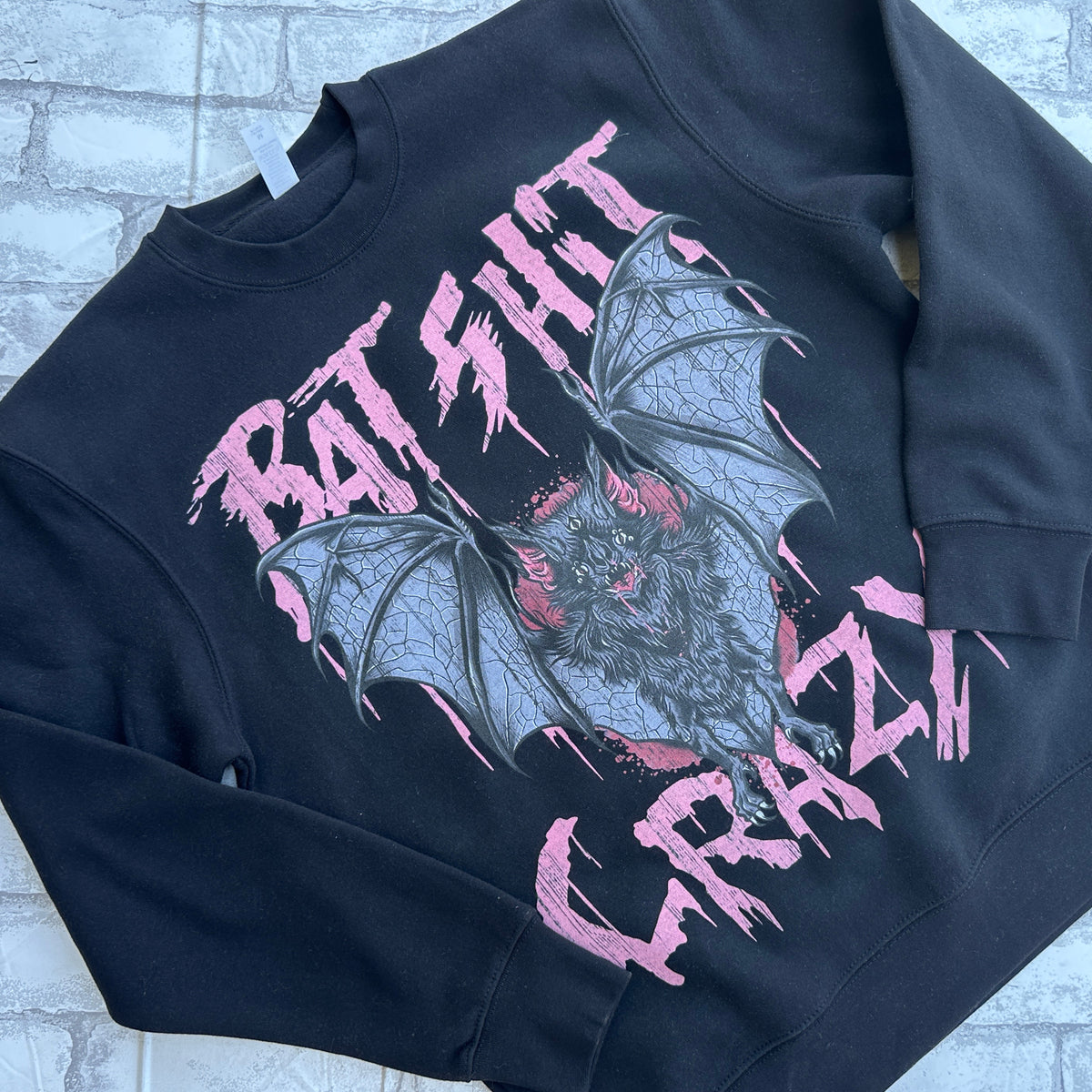 A black crewneck sweatshirt with a graphic print of bats and the text 'BAT SHIT CRAZY' in pink.