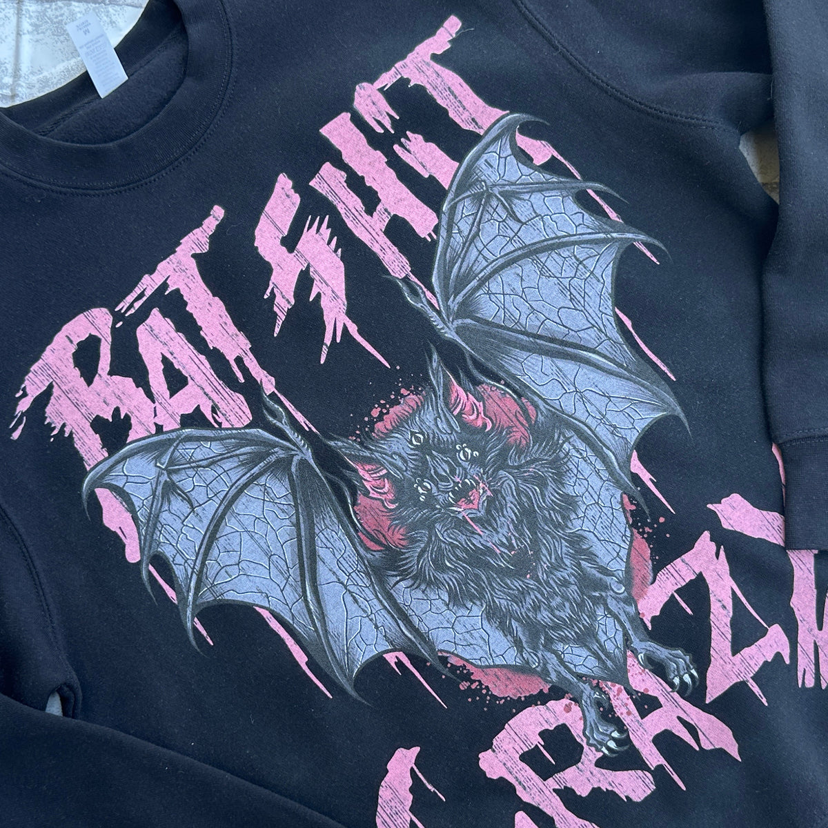 A black crewneck sweatshirt with a graphic print of bats and the text 'BAT SHIT CRAZY' in pink.