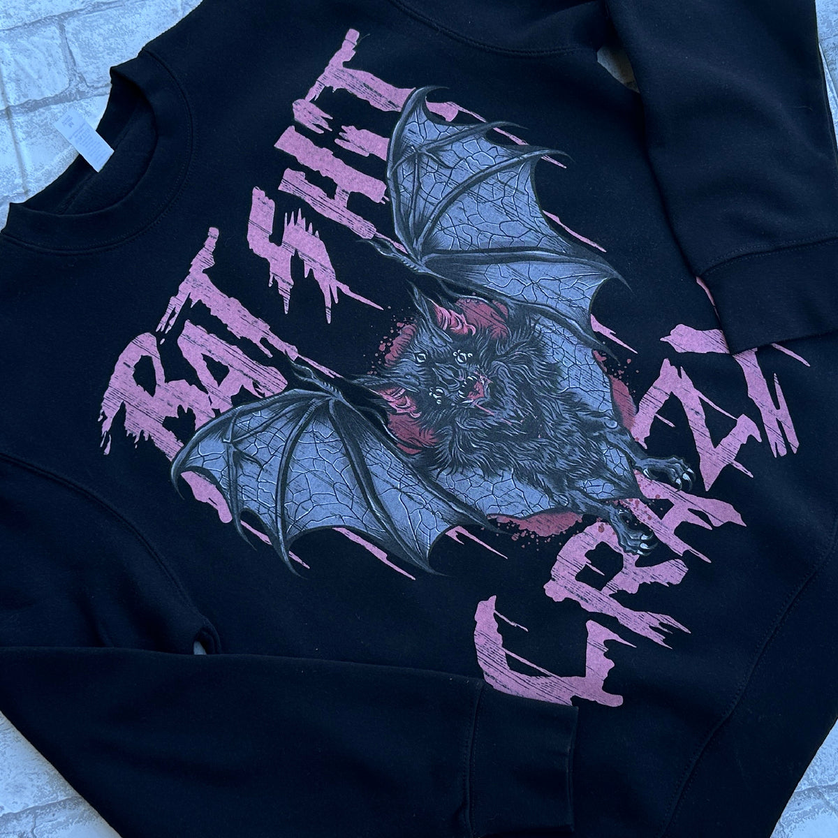 A black crewneck sweatshirt with a graphic print of bats and the text 'BAT SHIT CRAZY' in pink.