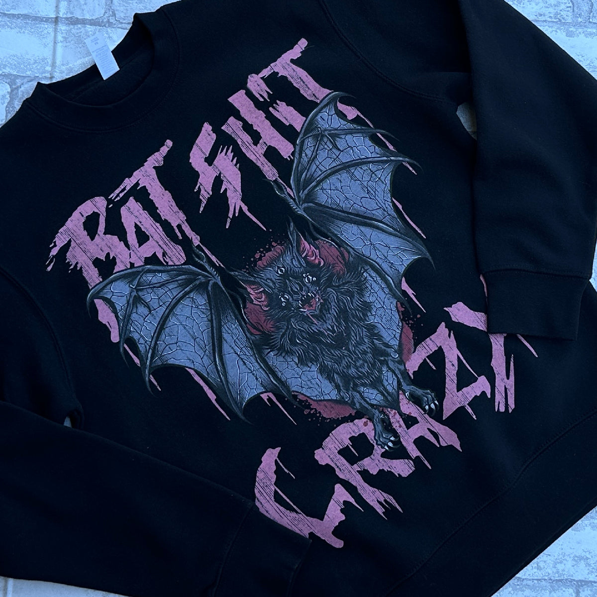 A black crewneck sweatshirt with a graphic print of bats and the text 'BAT SHIT CRAZY' in pink.