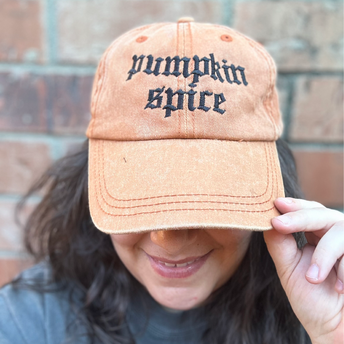 Pigment dyed Texas orange baseball cap with curved brim, featuring black embroidered text reading “pumpkin spice” on the front panel being modeled by female. 