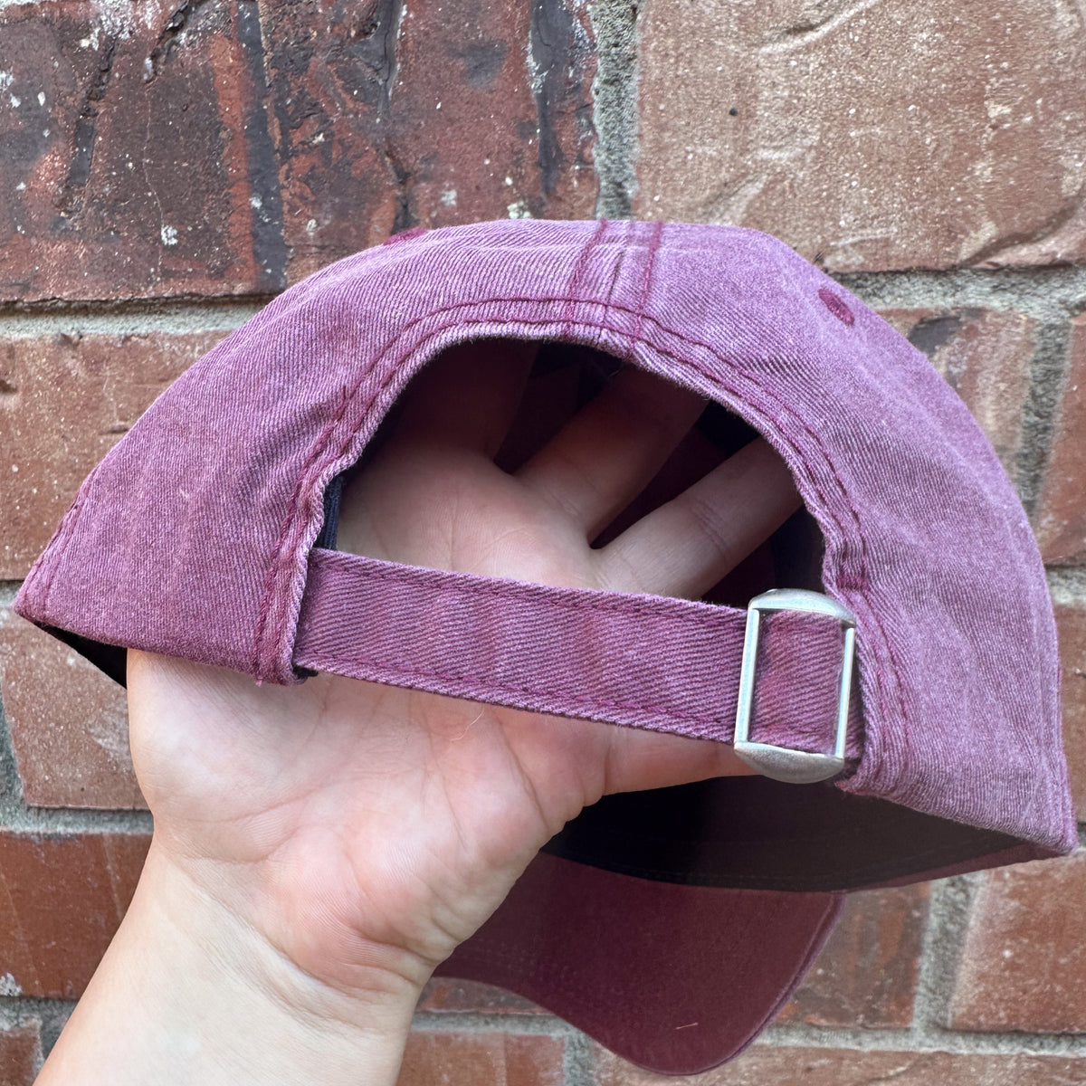 Back view of a distressed baseball cap showing adjustable fabric strap with metal buckle closure.