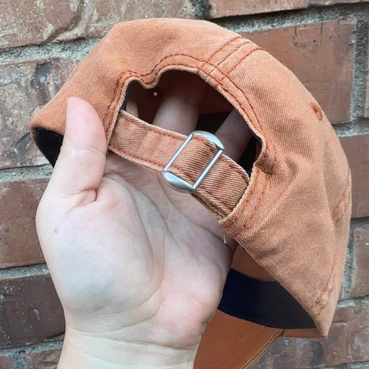 Back view of a distressed baseball cap showing adjustable fabric strap with metal buckle closure.