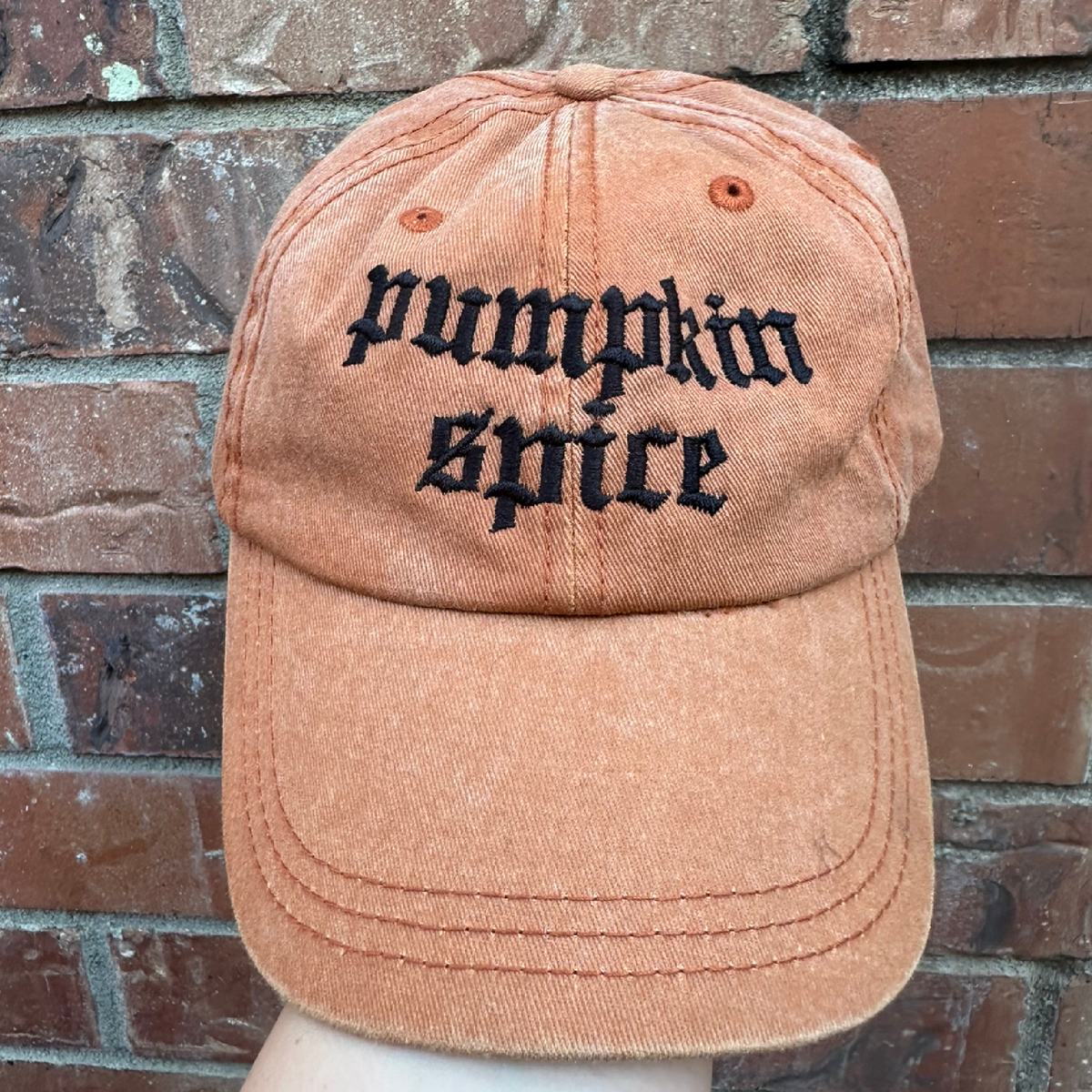 Pigment dyed Texas orange baseball cap with curved brim, featuring black embroidered text reading “pumpkin spice” on the front panel.