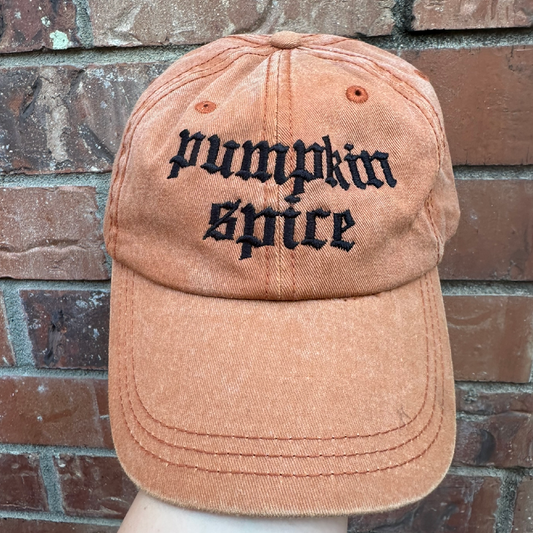 Pigment dyed Texas orange baseball cap with curved brim, featuring black embroidered text reading “pumpkin spice” on the front panel.