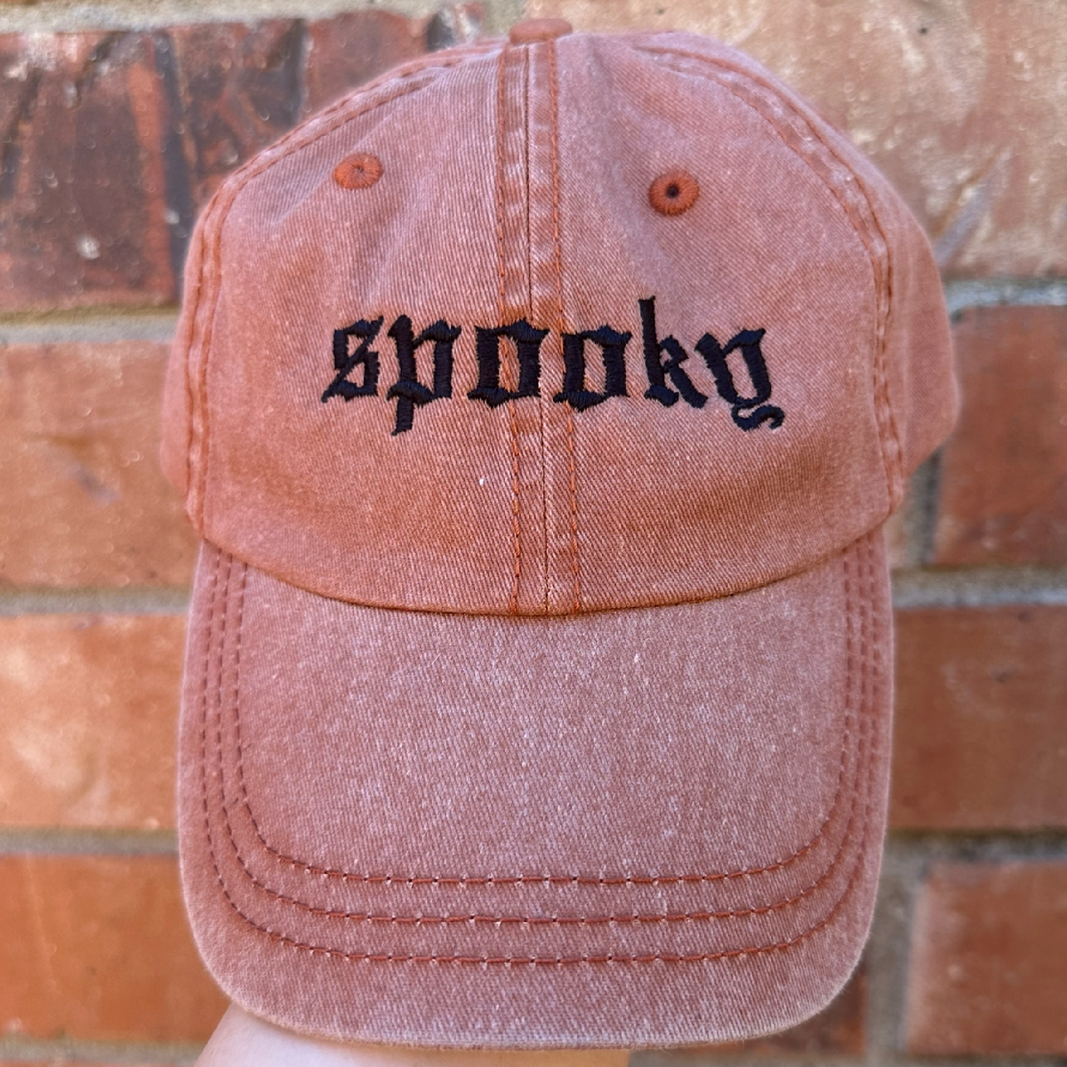 Pigment dyed Texas orange baseball cap with curved brim, featuring black embroidered text reading “spooky” on the front panel.