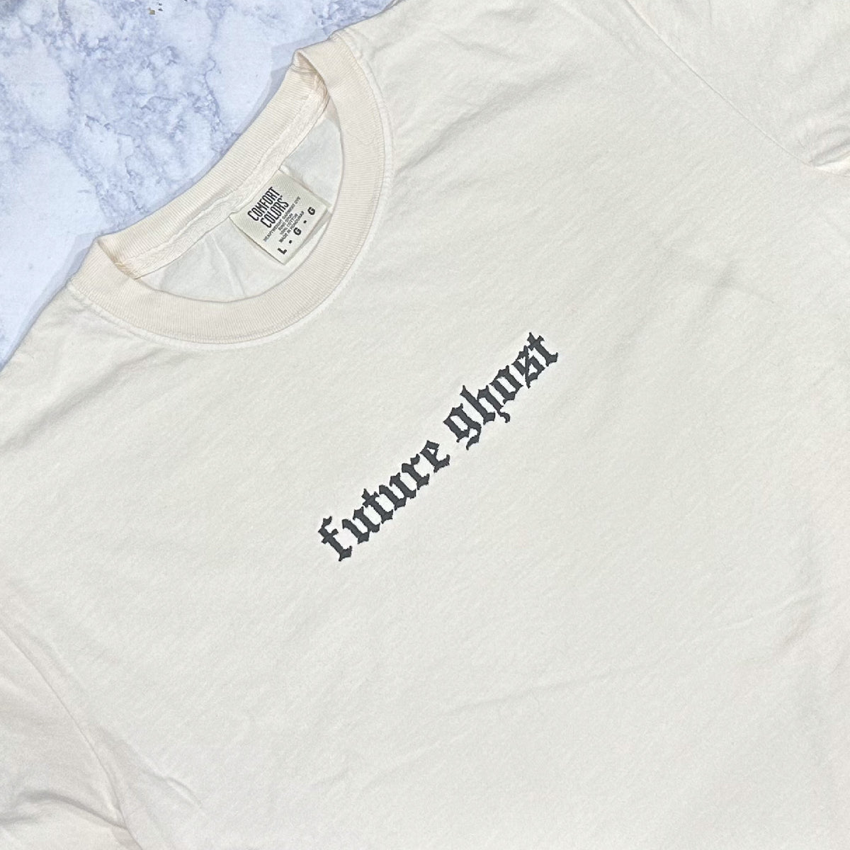 A cream Comfort Colors t-shirt with the text 'future ghost' embroidered in black thread on the front.