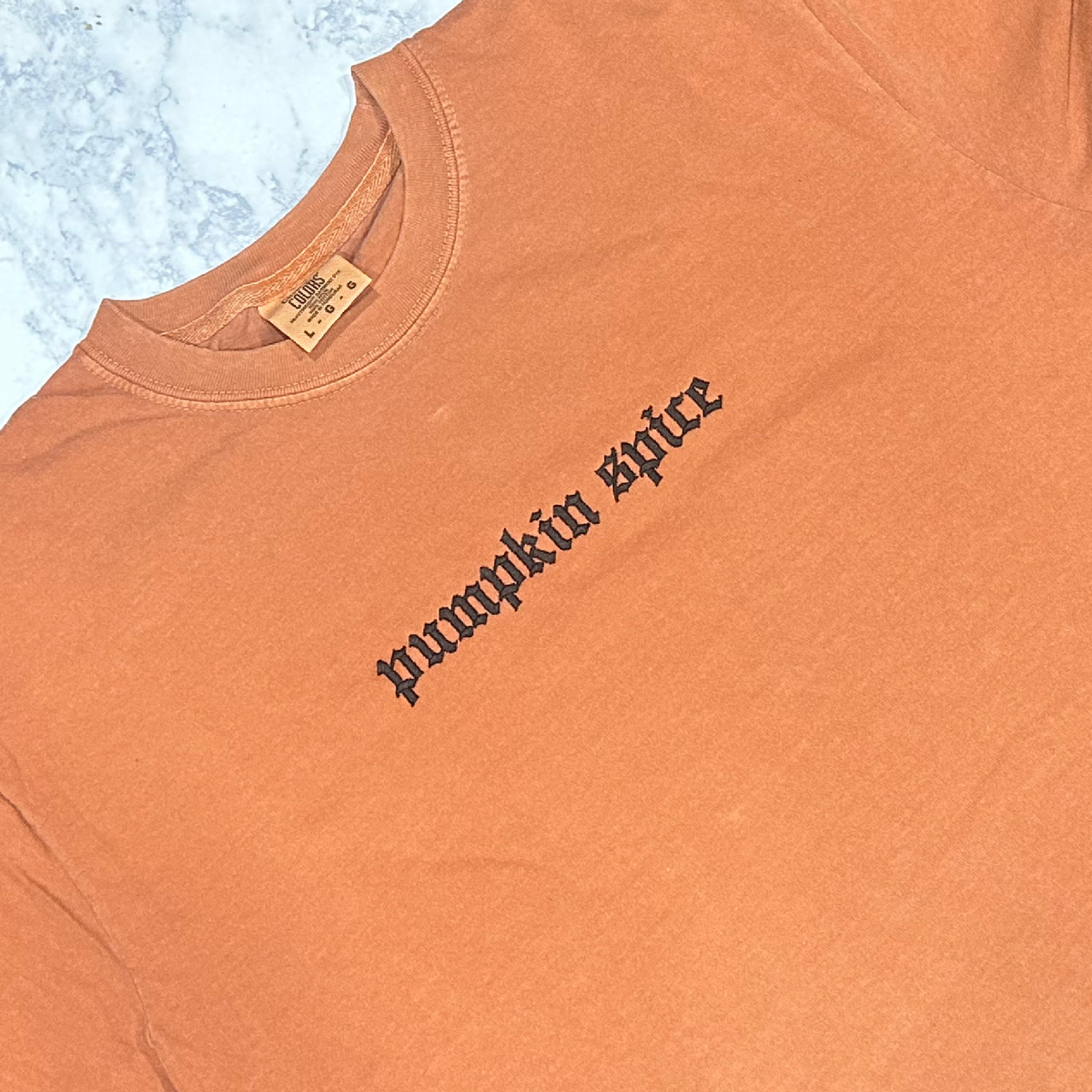 An orange t-shirt with 'PUMPKIN SPICE' embroidered in black thread.