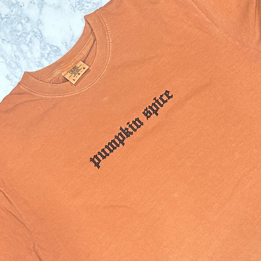 An orange t-shirt with 'PUMPKIN SPICE' embroidered in black thread.