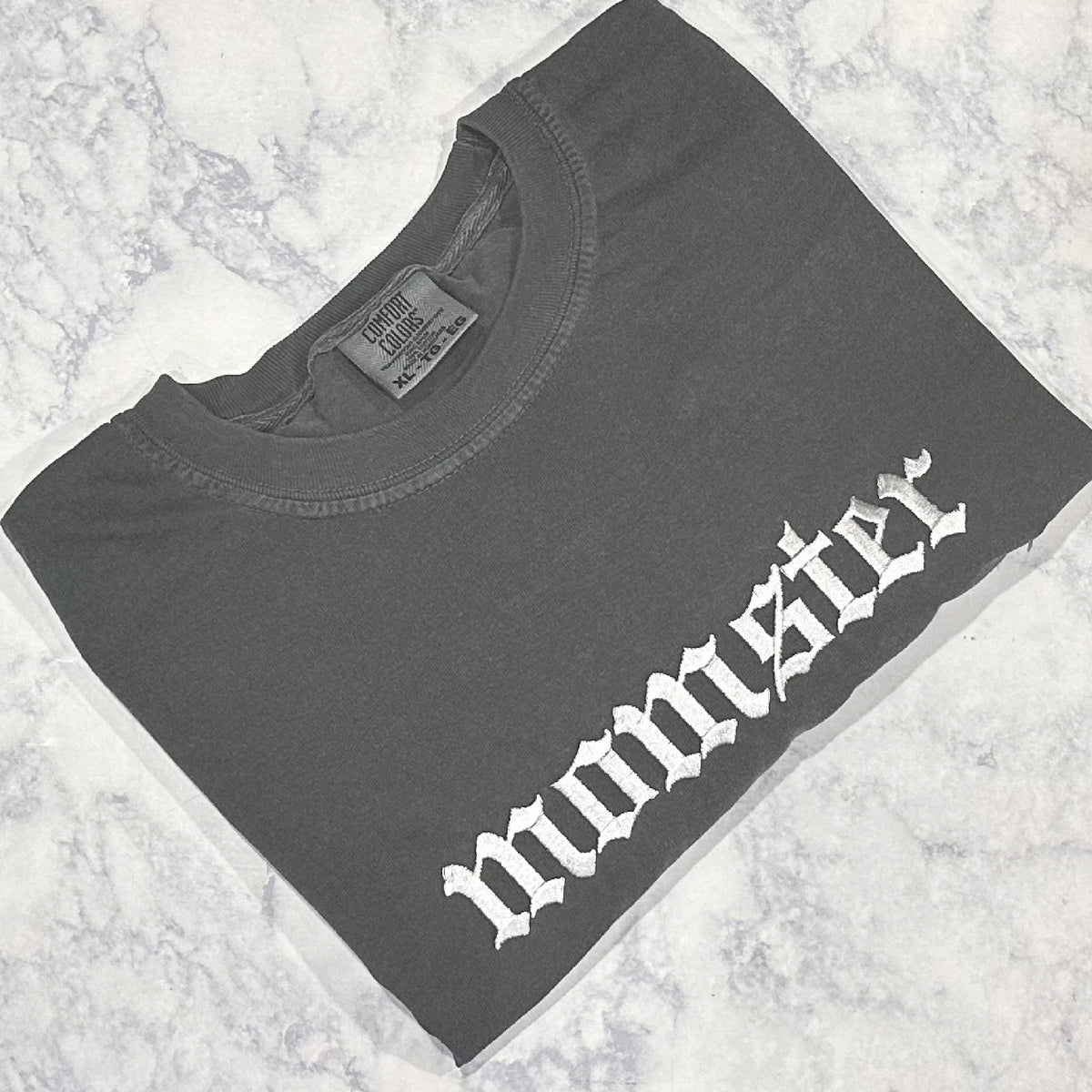 A pepper Comfort Colors t-shirt with the text 'momster' embroidered in white thread on the front.