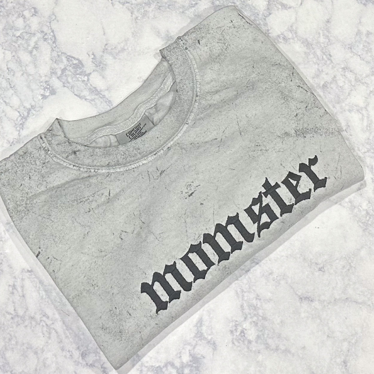 A Smoke Comfort Colors t-shirt with the word 'momster' embroidered in a stylized font.
