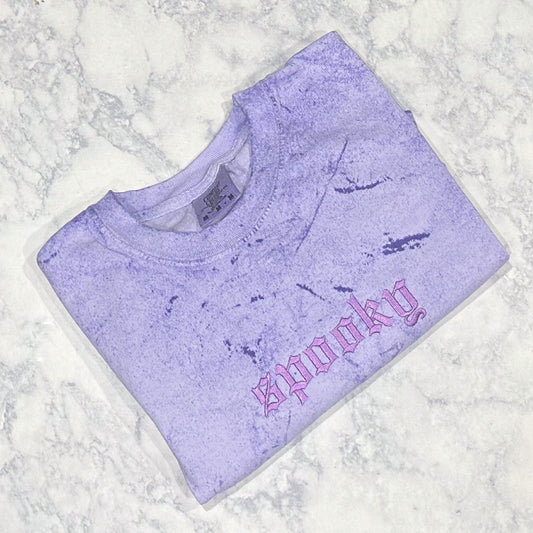 Light purple mineral-washed short-sleeve T-shirt laid flat, featuring small tonal embroidered text reading “spooky” on the chest.