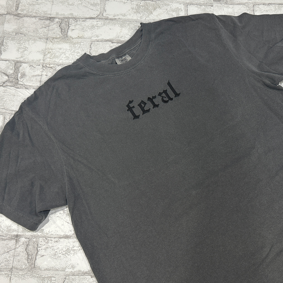 A pepper embroidered t-shirt with the word 'feral' written in bold letters across the front.