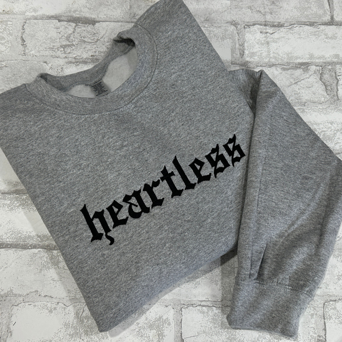 A gray crewneck sweatshirt with the word 'heartless' embroidered in black across the front.