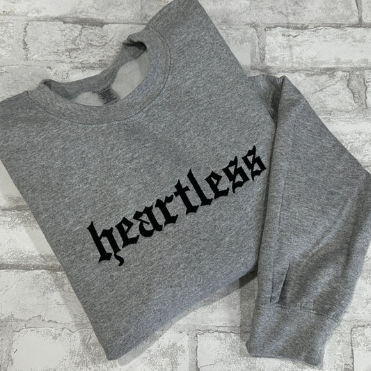 A gray crewneck sweatshirt with the word 'heartless' embroidered in black across the front.