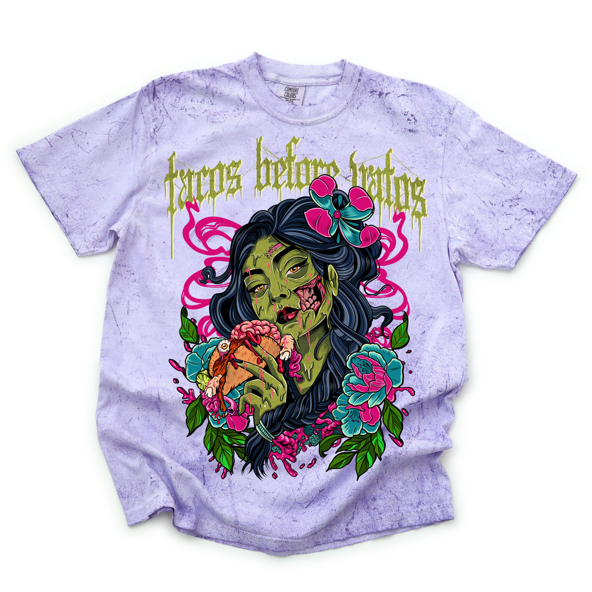The shirt is pigment dyed with a light purple shade with the phrase ‘Tacos Before Vatos’ above a colorful gothic illustration of a woman holding a taco surrounded by flowers