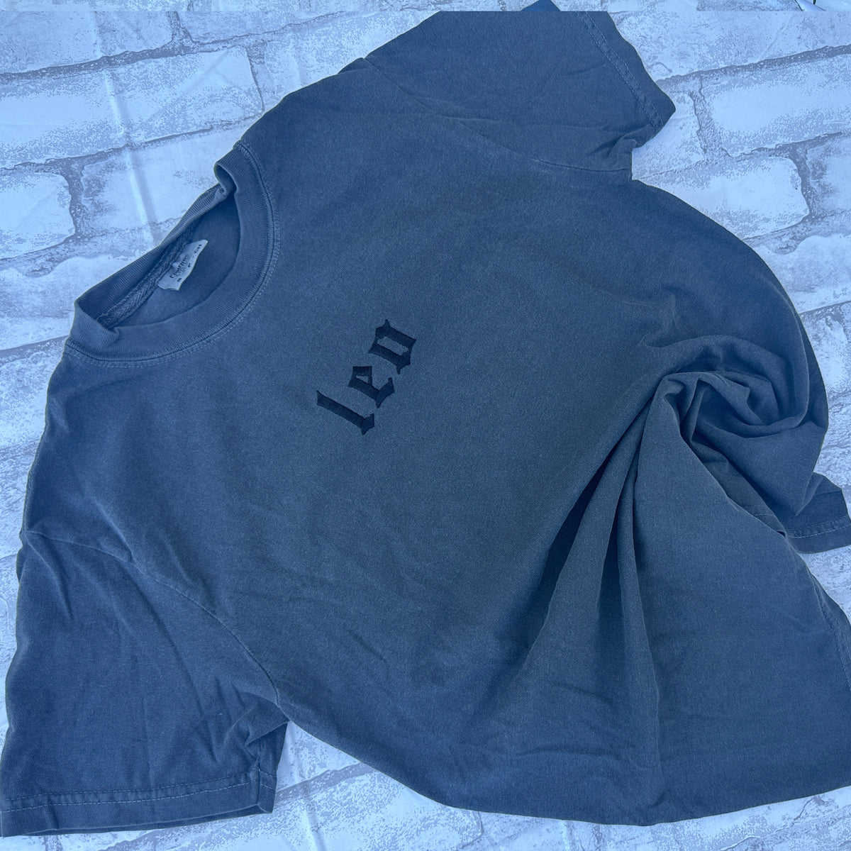 pepper colored comfort color t-shirts with embroidered leo zodiac signs displayed on a textured surface.