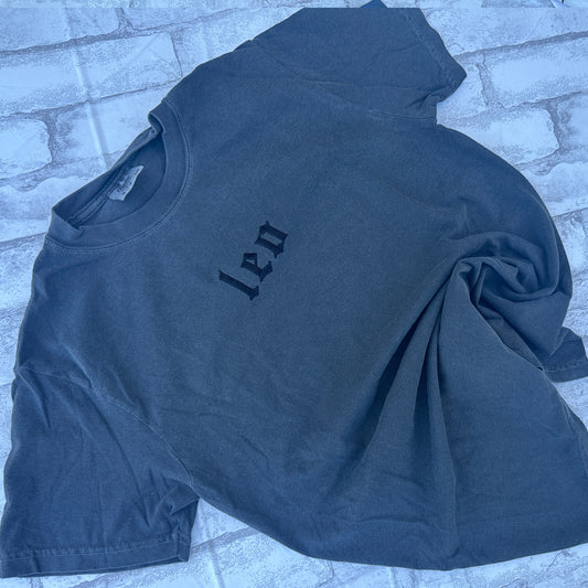 pepper colored comfort color t-shirts with embroidered leo zodiac signs displayed on a textured surface.