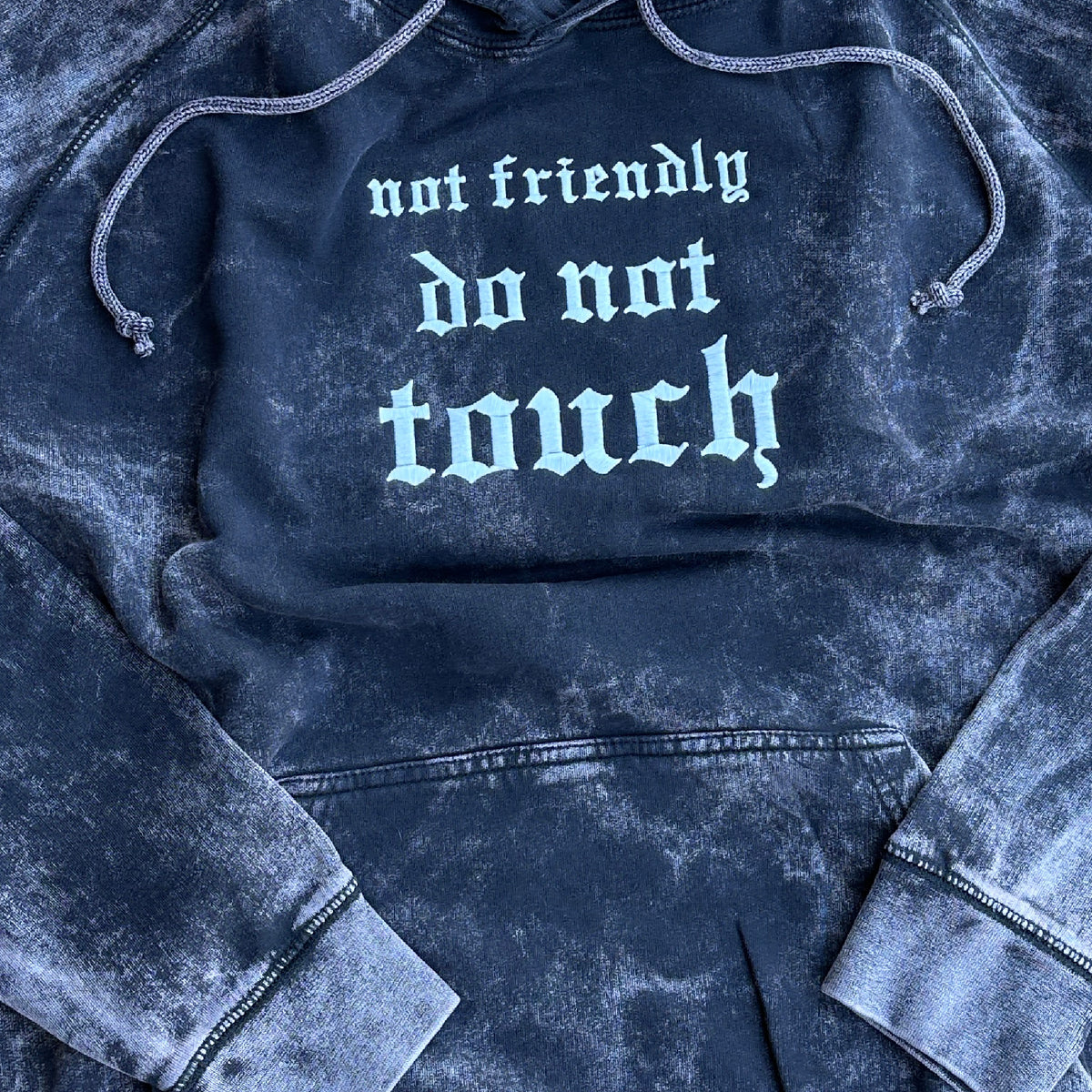 Vintage washed black pullover hoodie featuring white Old English embroidery that reads “not friendly do not touch” across the chest, with an adjustable drawstring hood, kangaroo pocket, and ribbed cuffs and hem.