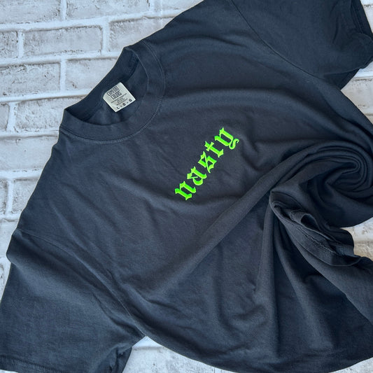 A black short-sleeve t-shirt with the word 'nasty' embroidered in a bright green gothic font across the chest, displayed flat against a white background.