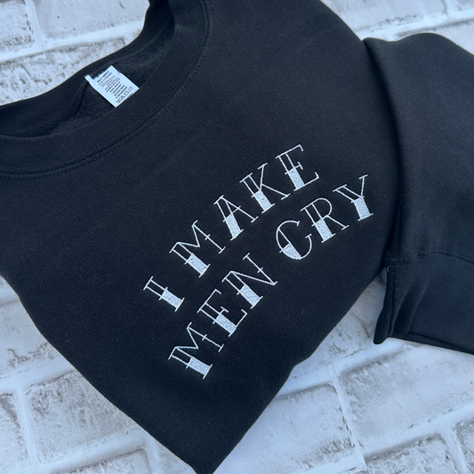 Black crewneck sweatshirt featuring white embroidered text across the chest that reads “I Make Men Cry” in a distressed vintage-style font, shown on a white background.