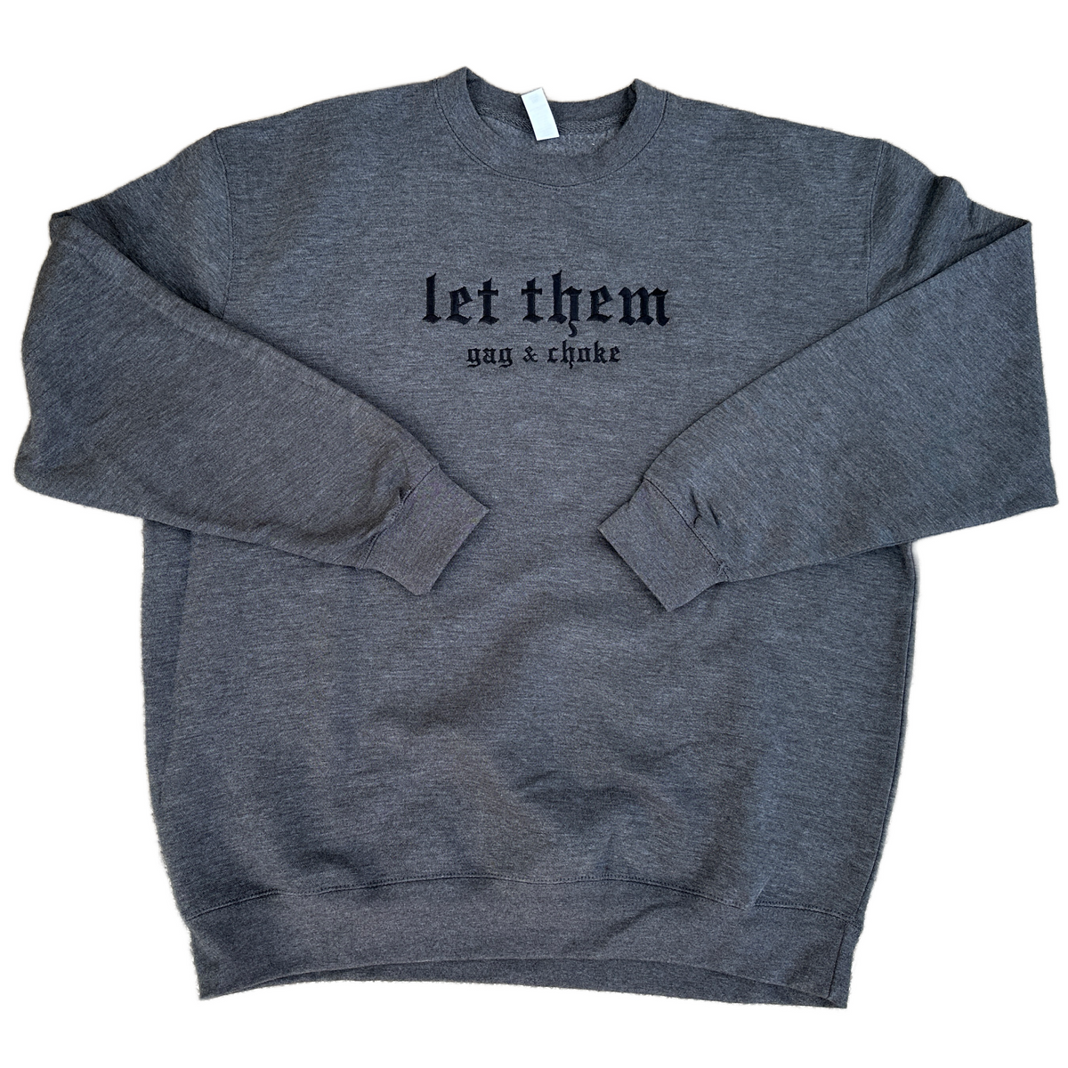 Dark Heather gray crewneck sweatshirt featuring black embroidered gothic text across the chest reading “let them” with smaller text underneath reading “gag & choke,” shown flat on a white background.