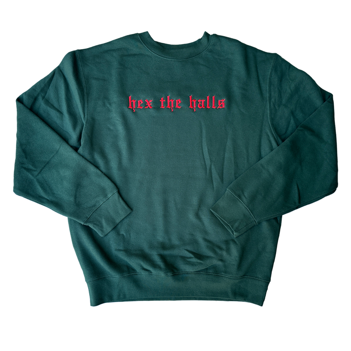 Dark forest green crewneck sweatshirt featuring red Old English gothic embroidery reading “hex the halls” across the upper chest. Long-sleeve pullover with ribbed cuffs, collar, and hem, displayed flat against a white background.