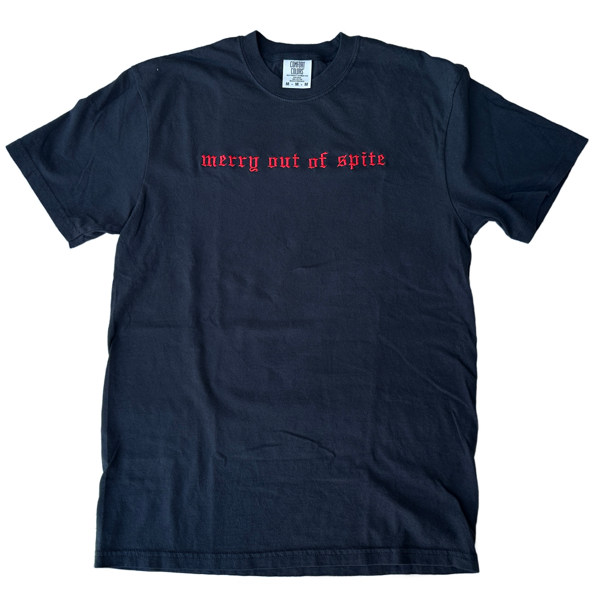 Black Comfort Colors short-sleeve T-shirt featuring red Old English gothic embroidery reading “merry out of spite” across the upper chest. Classic crewneck collar with a relaxed fit, displayed flat against a white background.